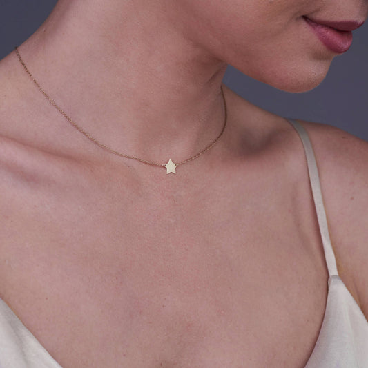 Primo piano di una donna che indossa una collana con stella in oro 14K.