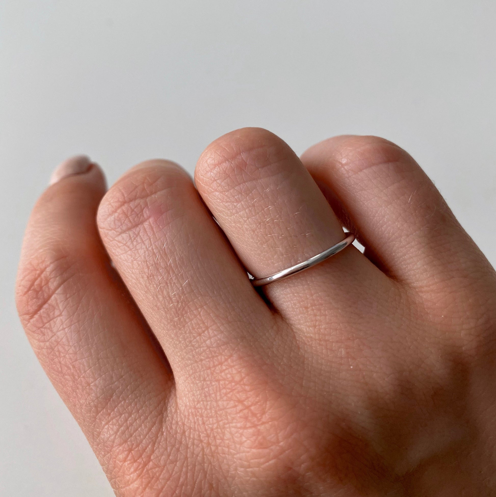 Una mano che indossa un semplice anello d'argento su uno sfondo chiaro.