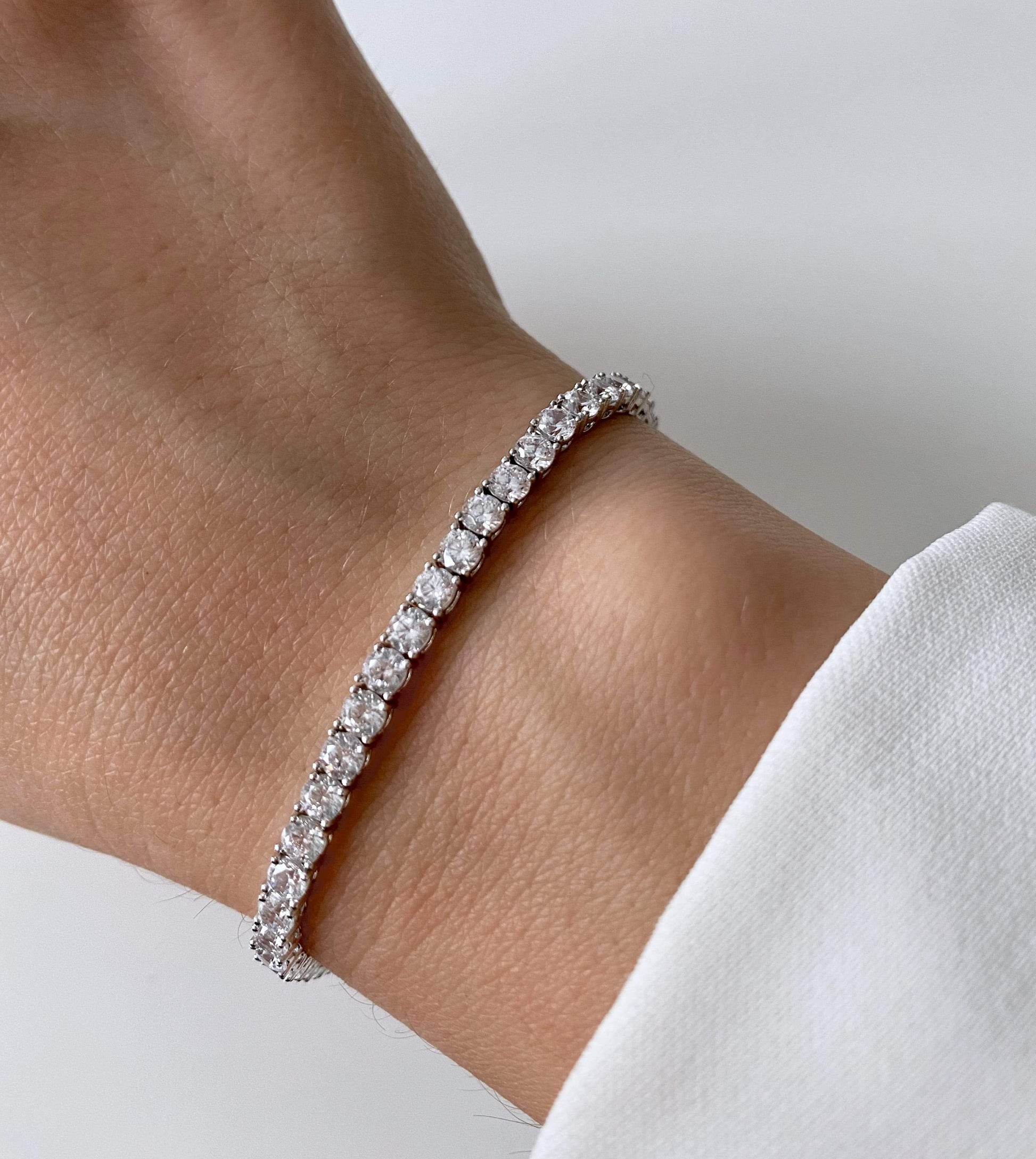 Primo piano di un polso che indossa un braccialetto tennis in argento con pietre di zirconia.