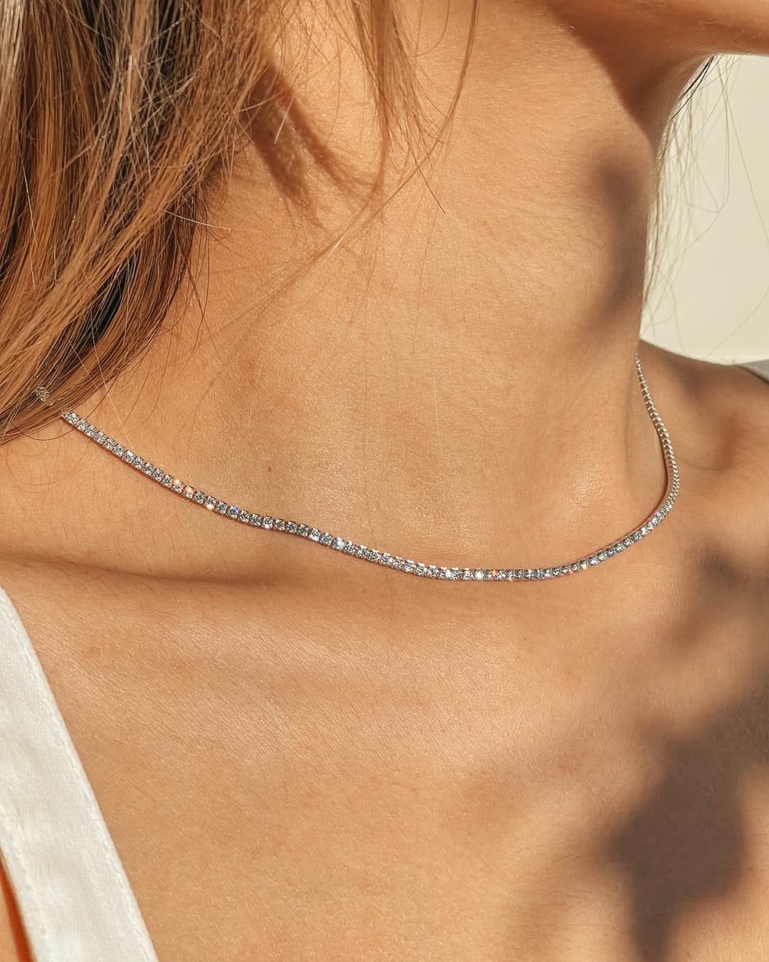 Primo piano del collo di una donna che indossa una collana tennis in argento con pietre di zirconi.
