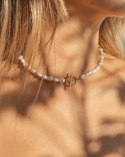 Primo piano di un collo femminile adornato con una collana d'argento con perle naturali e fermaglio in oro.